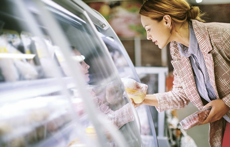 Frau nimmt Lebensmittel aus Kühlregal im Supermarkt