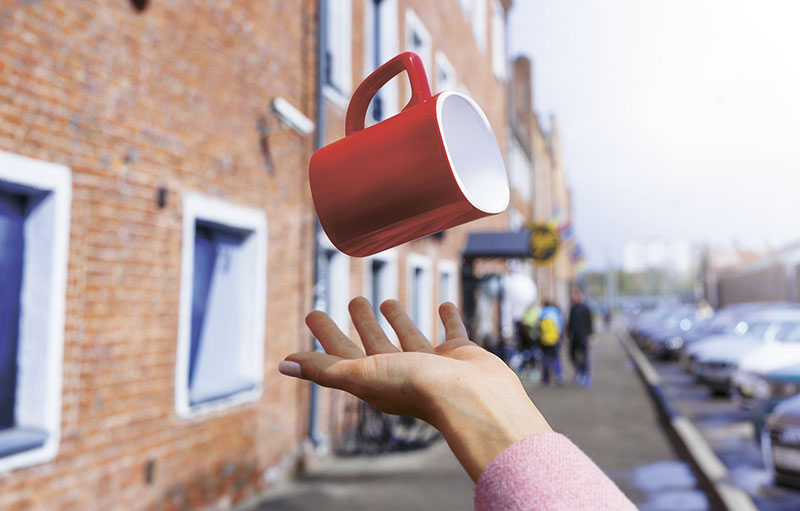 Weibliche Hand wirft auf Straße Tasse in die Luft