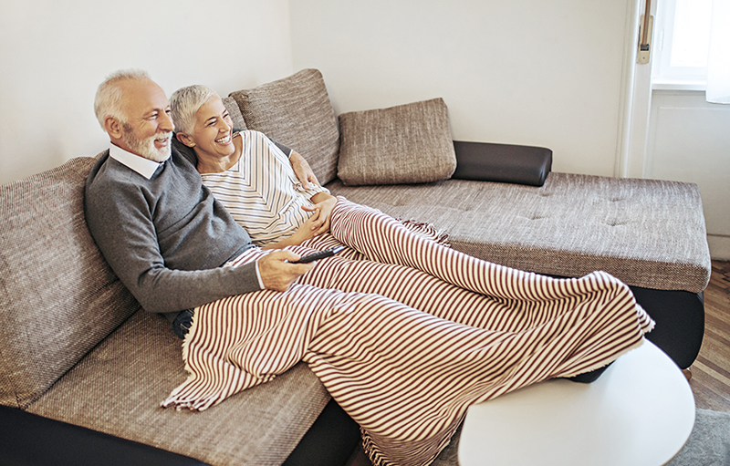 Älteres Paar sitzt mit Fernbedienung auf dem Sofa