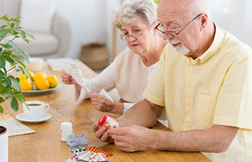 Älterer Mann und ältere Frau bereiten am Tisch ihre Pillenrationen vor