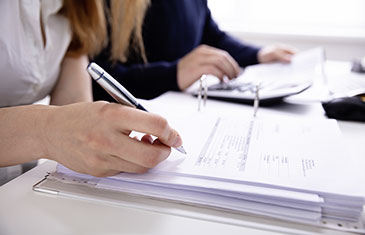 Foto zweier Menschen, die mit Taschenrechner und Stift Rechnungen kontrollieren. 