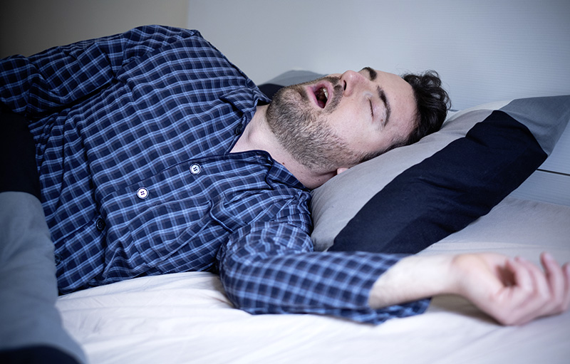 Foto von einem Mann im karierten Schlafanzug, der mit offenem Mund schläft