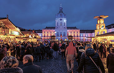 Foto von einem im Dunkeln hell erleuchteten Marktplatz mit Weihnachsmarkt, auf dem sich viele Menschen tummeln