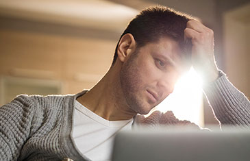 Foto von jungem Mann, der mit aufgestütztem Arm und ernster Miene auf den Laptop blickt