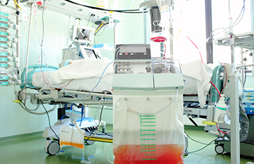 Foto von kaum sichtbarem Patient im Krankenhausbett umgeben von zahlreichen Apparaturen und Schläuchen