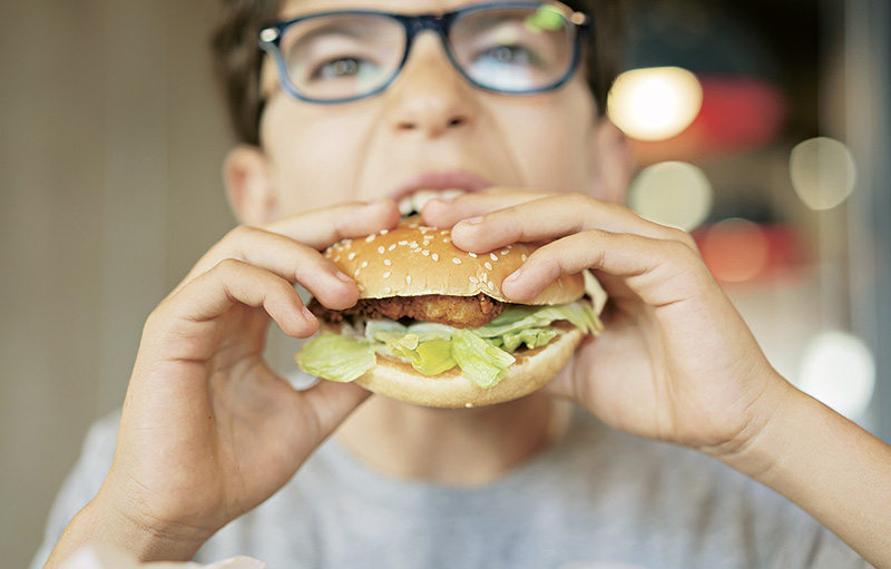Foto von Junge mit Brille, der herzhaft in einen Burger beißt