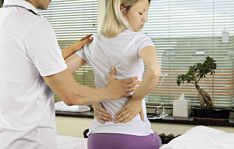 Foto von Arzt, der eine mittelalte Frau mit Rückenschmerzen untersucht