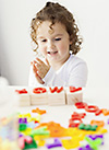 Foto eines kleinen Mädchens, das an einem weißen Spieltisch bunte Buchstaben aus Plastik sortiert