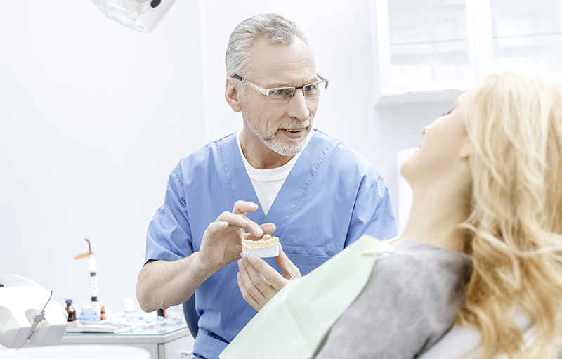 Foto von älterem Zahnarzt mit Gewbissabdruck in der Hand, der Frau auf Zahnarztstuhl berät