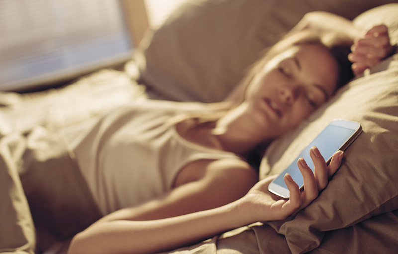 Junge Frau, die mit Smartphone in der Hand im Bett eingeschlafen ist