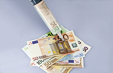 Foto einer mit Geldscheinen gefüllten Spritze, die in Geldscheine sticht