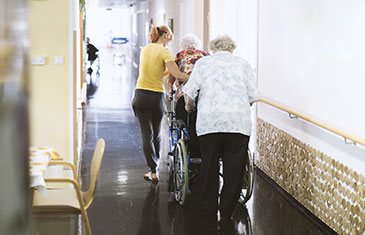 Foto von Flur einer Pflegeeinrichtung mit zwei alten Damen und Helferin
