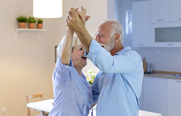 Foto eines fröhlich in einer Wohnung tanzenden älteren Paars