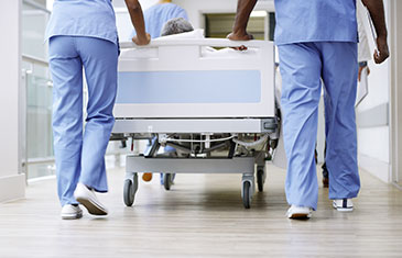 Foto eines Klinikbettes, das von medizinischem Personal durch den Krankenhausflur geschoben wird
