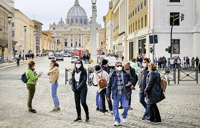 Menschen stehen, zum Teil mit Mund-Nasen-Schutz, auf dem St. Peters Platz in Rom.