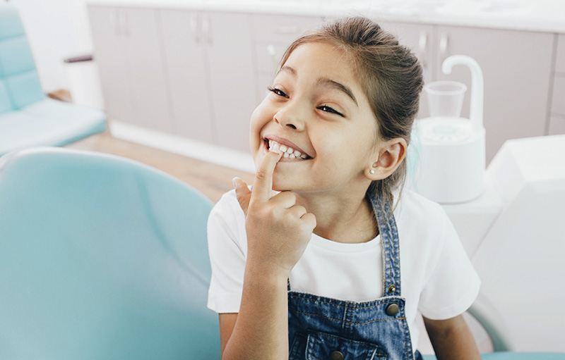 Foto eines kleinen Mädchens, das beim Zahnarzt seine Milchzähne zeigt
