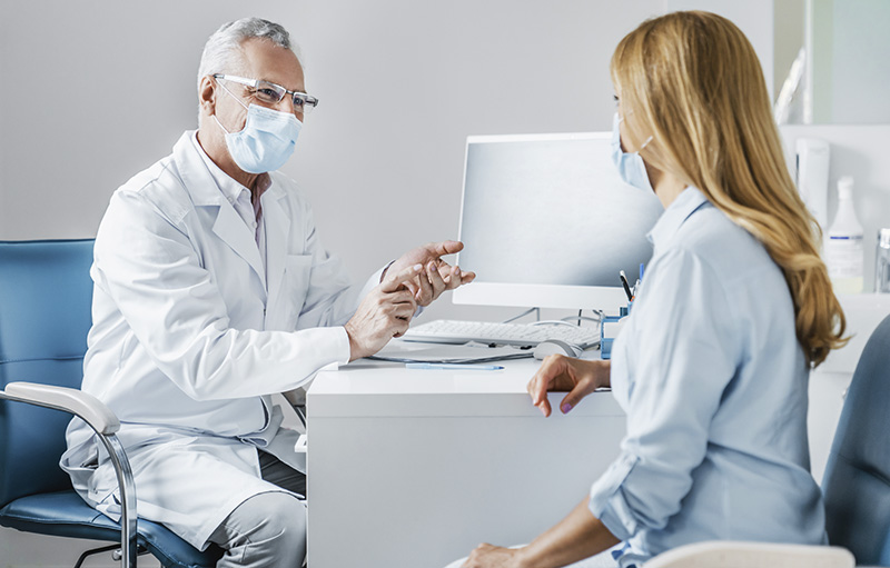 Foto einer Frau in der Beratung bei einem Arzt. Beide tragen Maske.