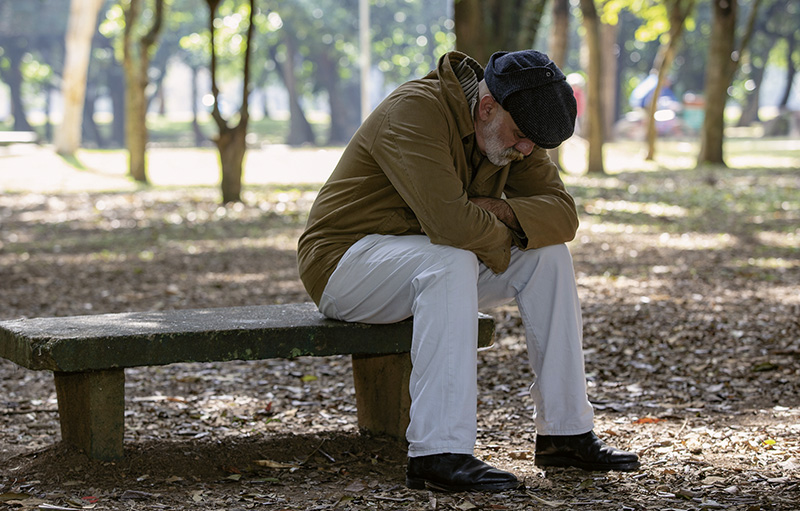 Foto eines alten Mannes, der gebeugt und traurig auf einer Bank im Park sitzt