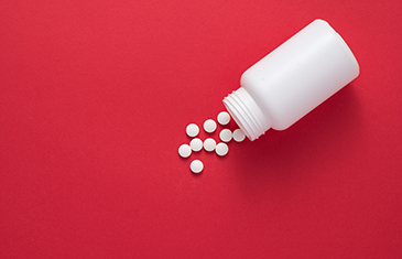 Foto eines weißen Tablettenschraubgefäßes aus dem ebenso weiße Tabletten fallen vor rotem Hintergrund