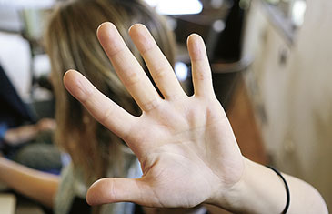 Foto einer Frau, die schützend die Hand vor ihren Kopf hält und das Gesicht abwendet
