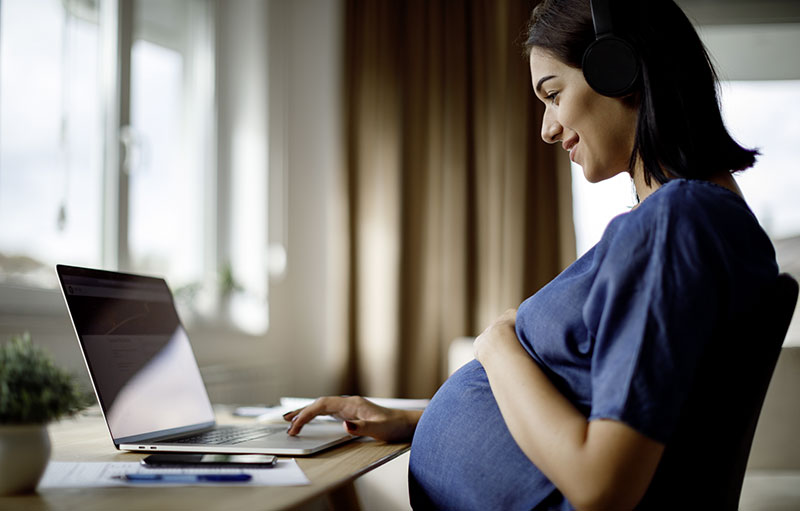 Foto einer schwangeren Frau, die vor einem Laptop sitzt