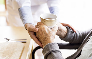 Foto eines älteren Menschen, der Unterstützung beim Trinken von einer Pflegekraft erhält. Man sieht jeweils nur die Hände.