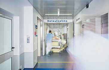 Foto eines Krankenhausflurs, durch den ein Patientenbett in Richtung Notaufnahme geschoben wird