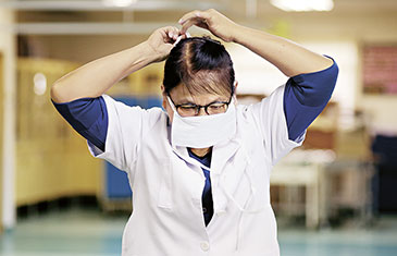 Foto einer älteren Pflegerin in weißem Arbeitskittel, die sich eine Maske umbindet