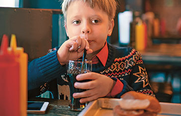 Foto eines kleinen Jungen, der Cola trinkt, vor ihm steht ein Burger