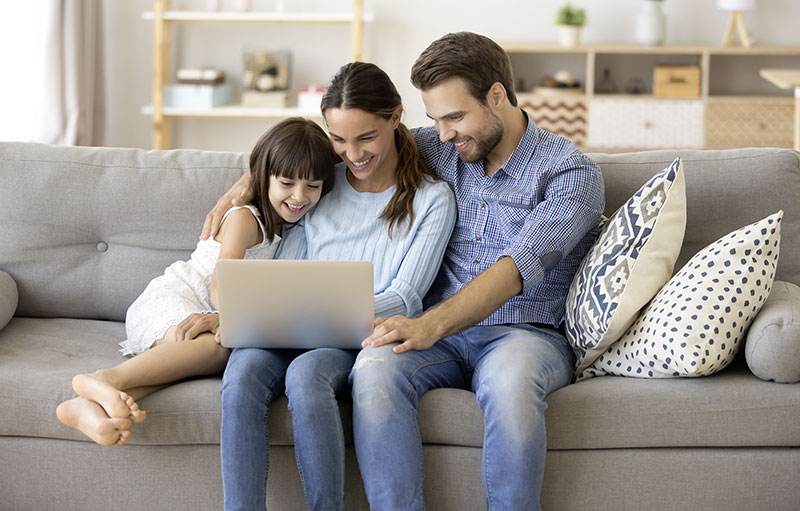Foto von Vater, Mutter und Kind vor einem Laptop, die gemeinsam auf dem Sofa sitzen