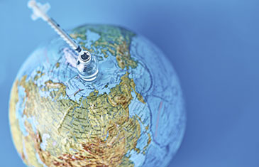 Symbolbild: Globus, auf dem eine Impfdosis mit Spritze darin steht
