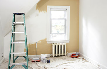 Foto eines renovierungsbedürftigen Zimmers mit Leiter und Streichutensilien