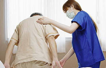 Foto einer Pflegerin mit Maske, die einem alten Mann hilft