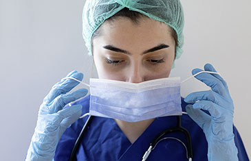 Foto einer Pflegerin in Schutzkleidung, die sich ihre Maske anlegt