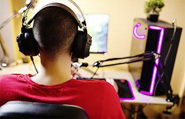 Foto eines Jungen von hinten mit Kopfhörern, der vor einem Gaming-Computer sitzt