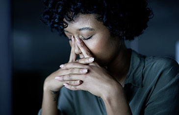 Foto einer verzweifelten Frau mit dunkler Hautfarbe vor schwarzem Hintergrund