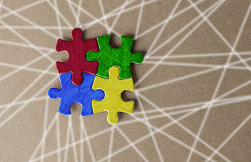 Symbolbild von vier Puzzleteilen, die ineinander gesteckt sind. Sie haben die einzelnen Farben Rot, Grün, Blau und Gelb. Darunter befinden sich weiße, gerade Linien, die das Bild von verschiedenen Seiten durchziehen.