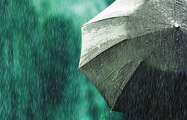 Foto eines Regenschirms von hinten bei strömendem Regen vor grünem Hintergrund im Freien