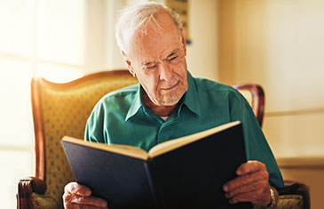 Foto eines alten Mannes, der auf einem Sessel sitzt und in einem Buch liest