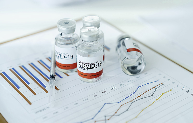 Foto von Covid-19 Impfdosen mitsamt Spritze, die auf einer wissenschaftlichen Auswertung mit Grafiken stehen