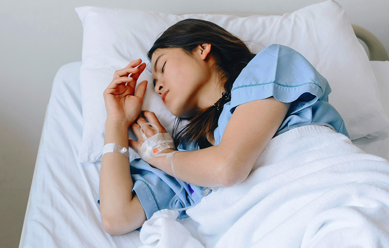 Bild einer jungen Frau, die mit Zugängen schlafend in einem Krankenbett liegt