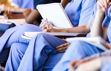 Foto von sitzenden Menschen in blauem Pflegekittel mit Fortbildungsunterlagen