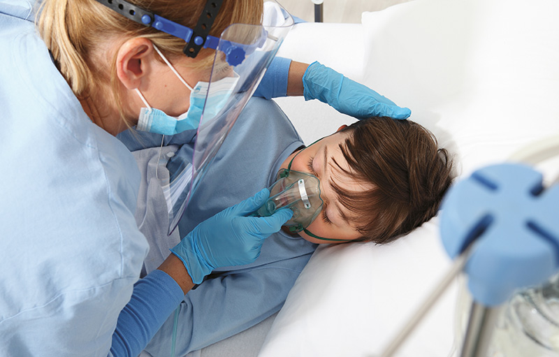 Foto einer Intensiv-Pflegerin mit Schutzausrüstung. Sie hält einem Kind eine Beatmungsmaske auf das Gesicht.