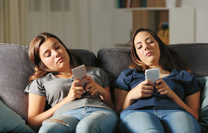 Foto von zwei jungen Frauen, die gelangweilt mit Smartphone auf dem Sofa abhängen