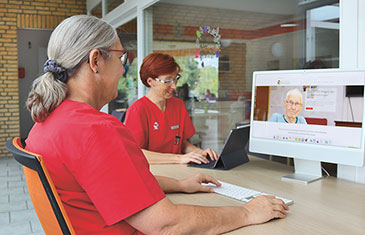 Foto von Pflegekräften am Schreibtisch vor Computer und Laptop