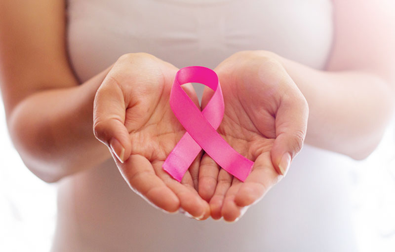 Symbolbild von zwei zur Schale geformten weiblichen Händen, die eine rosafarbene Brustkrebsschleife halten