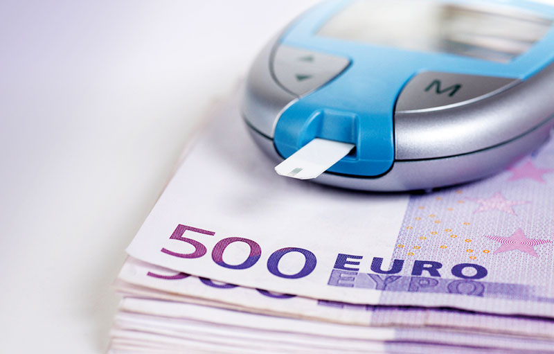 Symbolbild von 500-Euro-Geldscheinen, auf denen ein Blutzuckermessgerät liegt