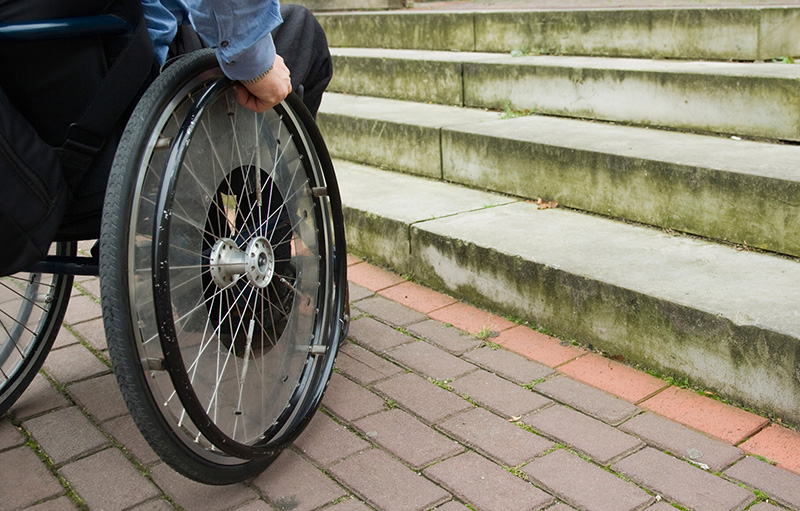 Foto eines Rollstuhlfahrers, der vor einer Steintreppe steht