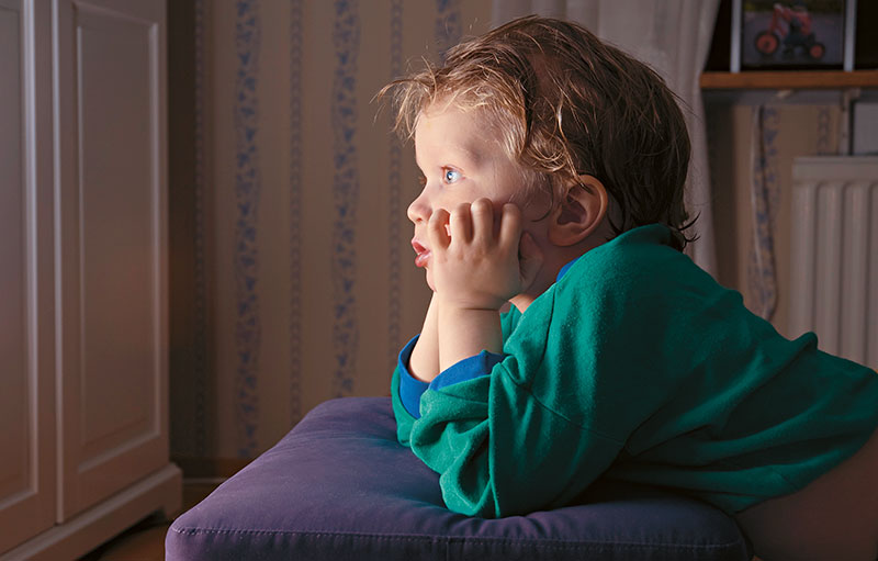 Symbolbild eines Kleinkindesm das in einem abgedunkelten Zimmer gebannt in den Fernseher starrt