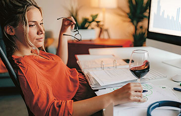 Symbolbild einer Frau mit einem Glas Rotwein am heimischen Computer